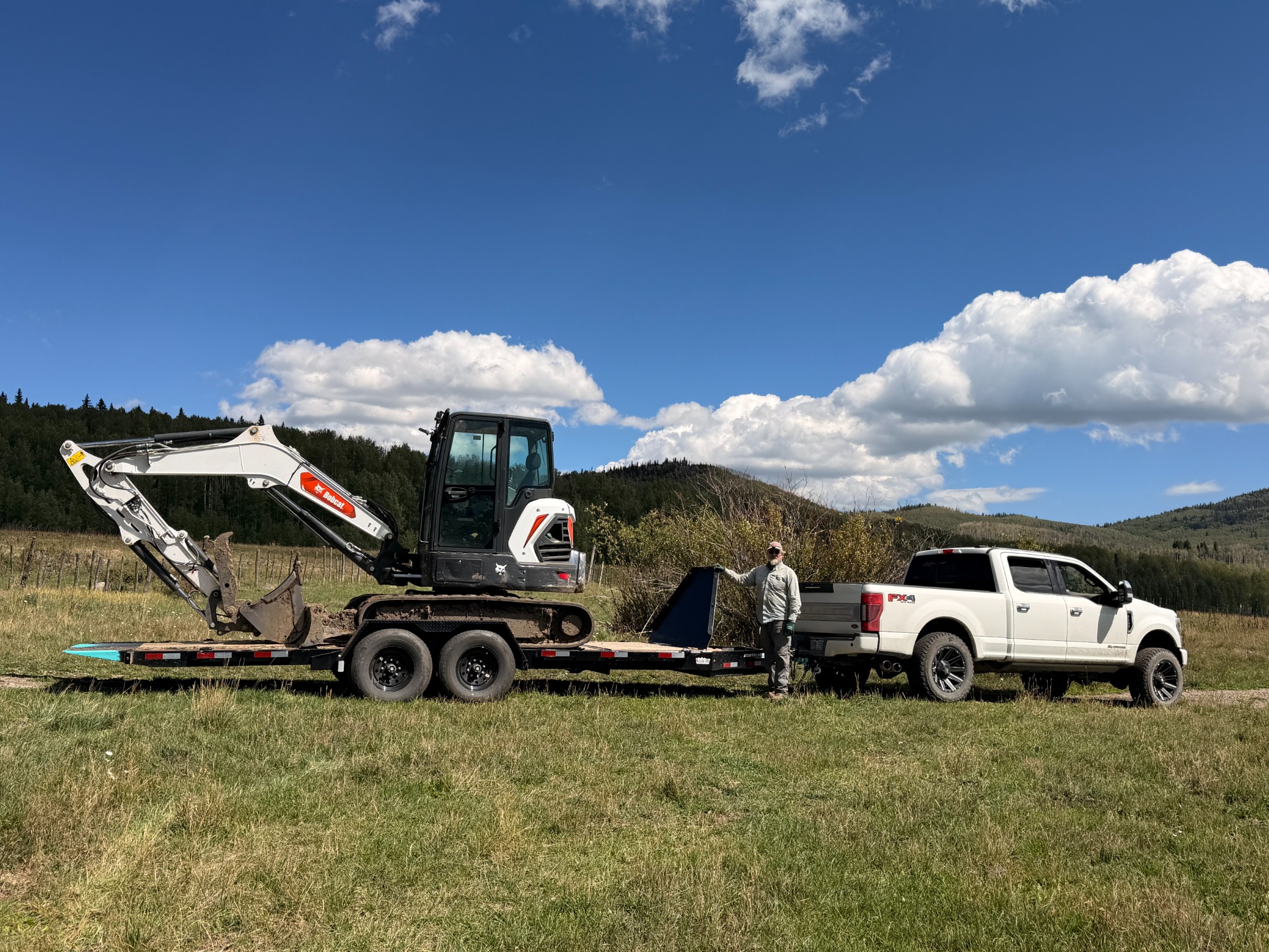 Edward Hokanson, owner-operator of HLS Project Management LLC, standing beside a white work truck, trailer and Bobcat excavator in Western Colorado